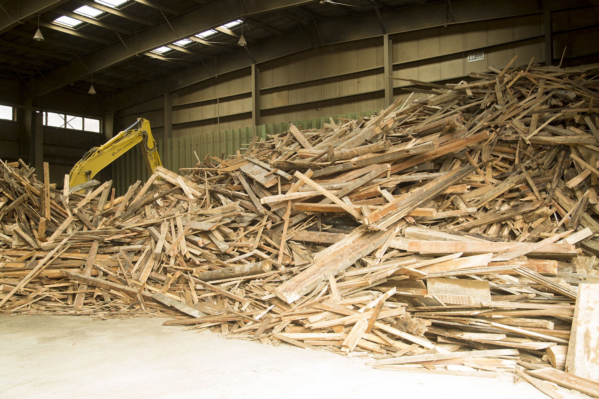 リサイクル炭化プラントに持ち込まれた廃材の山（上段）と、用途別に3段階に粉砕されたチップ（下段）。このうち7割が炭八の材料として炭化炉に回される