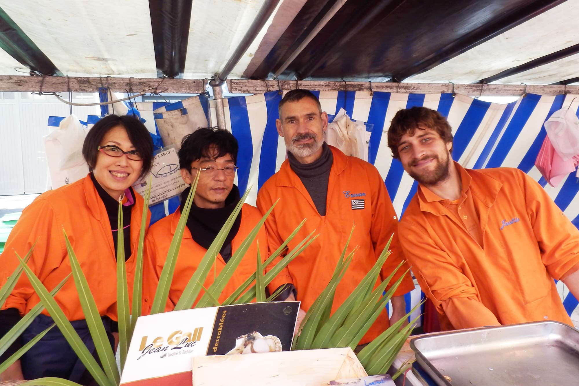 エルワン・ランシュー（写真右から2人目。左は日本から来仏した中谷紀人さん）／2007年よりパリのマルシェで、妻・森田晃子さん（左端）と鮮魚店を営む。現在は、週末のマルシェ11区と16区で魚介類を販売している。晃子さんとの出会いは、調理師免許を持つ晃子さんが渡仏して、フランス料理をコルドンブルー校で学んでいた時に、魚をさばく技術を教えてくださったのがエルワンさんだったこと。晃子さん手作りの握り寿司やお惣菜も大好評