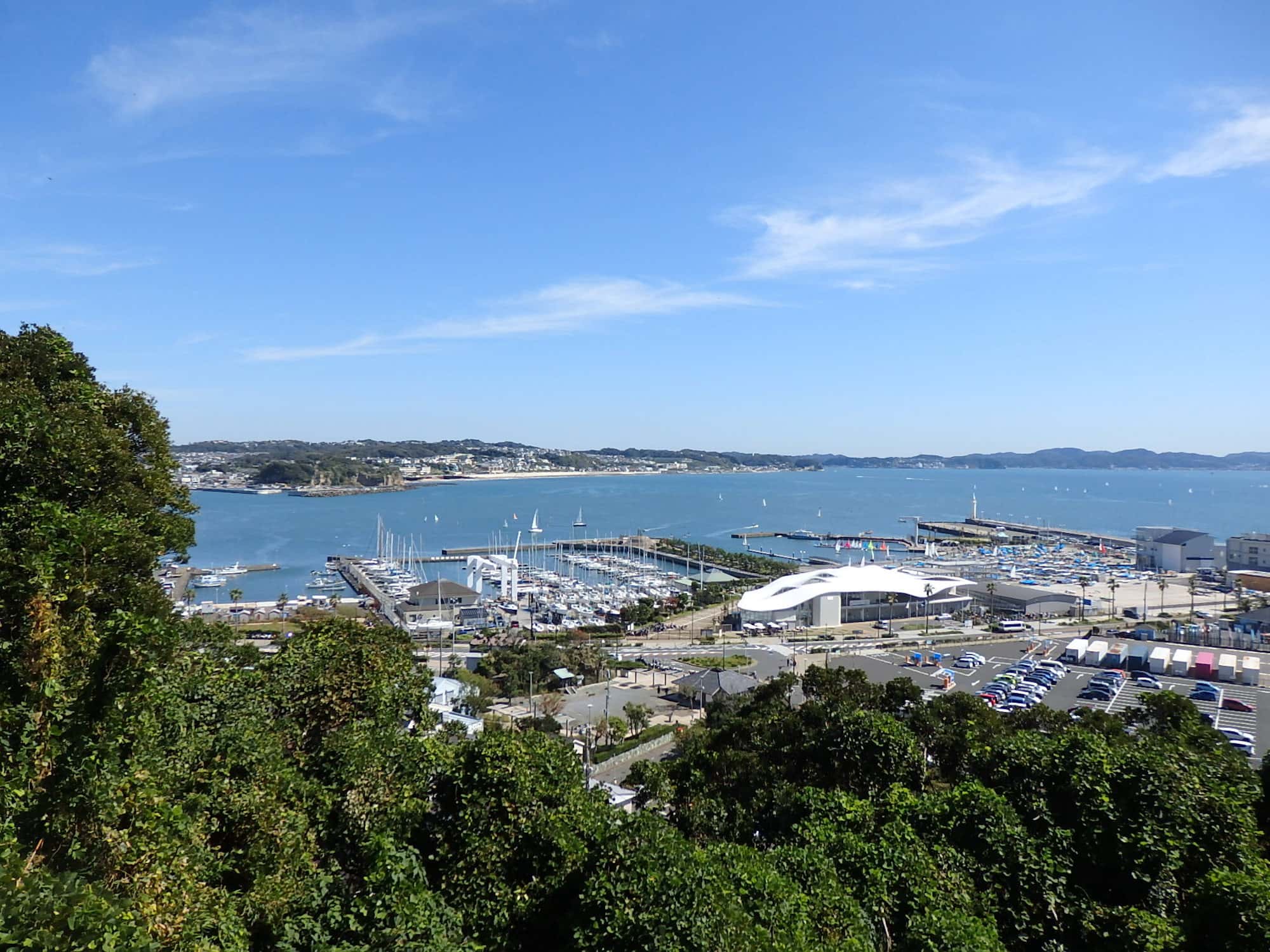 昭和39年（1964年）に東京オリンピックのヨット競技場として整備されたヨットハーバー。海を隔てた奥の中央付近が七里ヶ浜や由比ヶ浜、さらに右手奥には三浦半島の山並みが見える