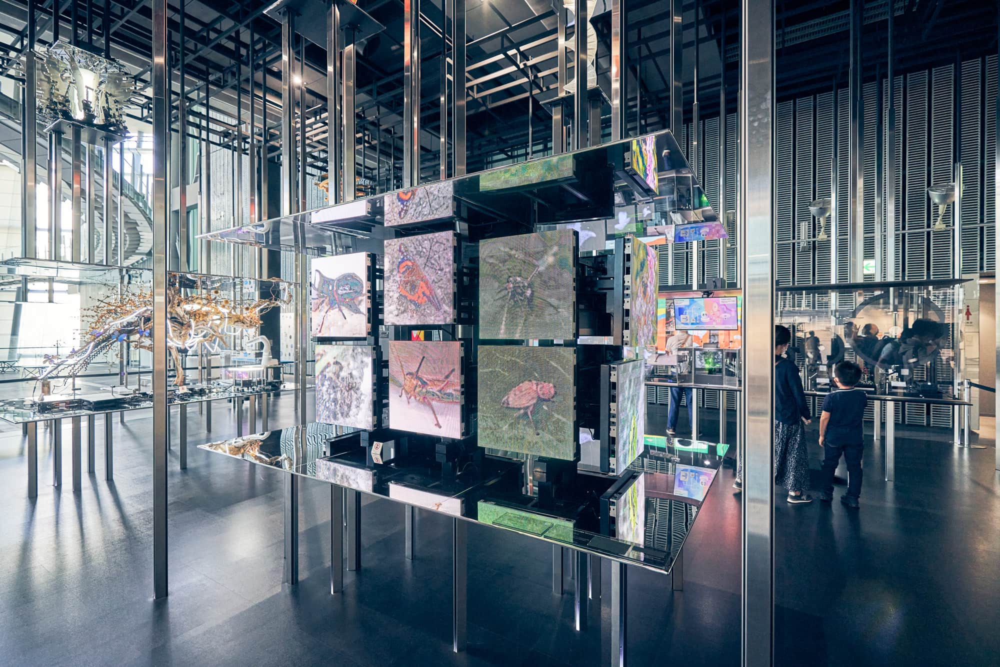 もう1つのシンボル展示「計算機の自然」。人工知能が、たくさんの画像の集まりからその特徴を認識して新たな画像を生成する。GAN（敵対的生成ネットワーク）とよばれる人工知能の学習システムを応用。生成器が偽データをつくり、識別器が本物のデータをもとにそのデータの真偽を判定することを繰り返して学習を進めることで、より本物に近い偽物を生成できるようになる。「自然は私たちが解釈するもの」と捉えがちだが、計算機は人間が知覚できる以上に特徴を認識しており、「計算機から見た自然」もありえるというコンセプト